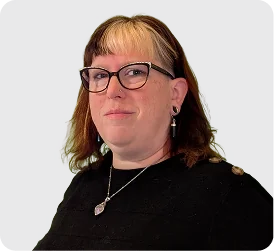 Woman with glasses and reddish-brown hair wearing a black top and a necklace, posed against a light gray background