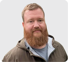 Man with a full red beard and blond hair wearing a brown jacket over a gray shirt