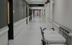 Empty hospital corridor with a gurney parked along the right wall under bright overhead lighting