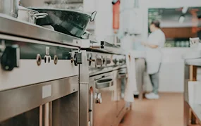 Stainless steel commercial kitchen equipment lines a professional restaurant kitchen with a chef working in the background