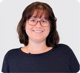 Smiling woman with short brown hair and red-framed glasses wearing a dark navy sweater
